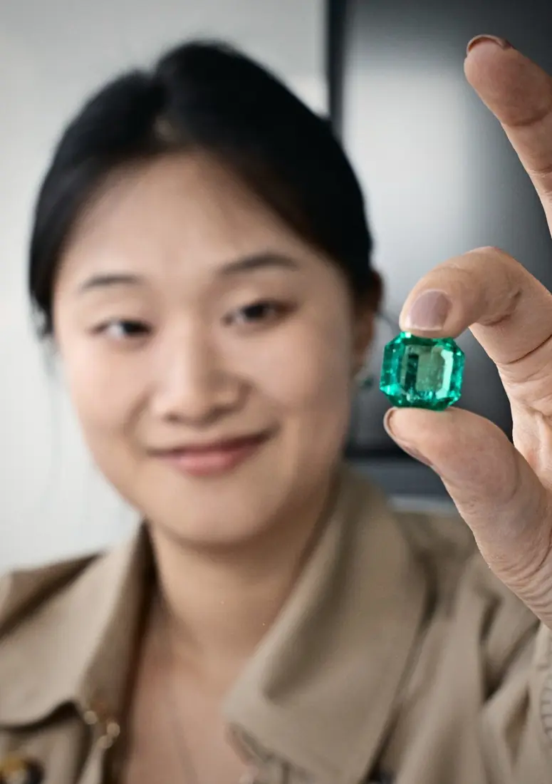 A client holds a cut emerald up to the light
