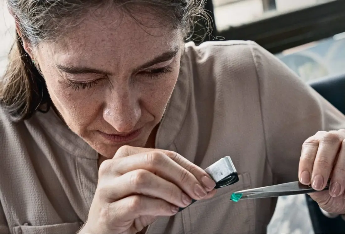 A gemmologist examines an emerald with a loupe and tweezers