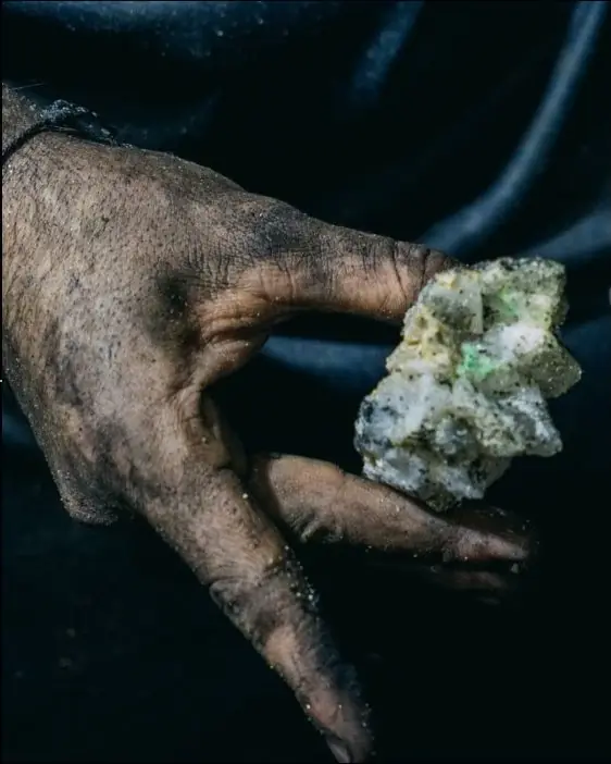 A miner's hand holding rough emerald in matrix